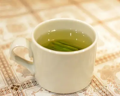 white cup of lemongrass tea with floating stalks, placed on a lace-patterned tablecloth
