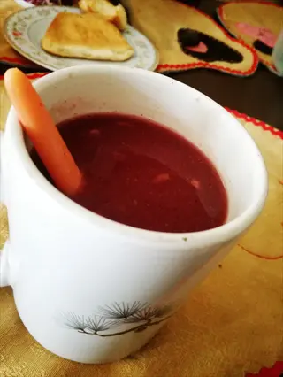 white mug filled with purple tomato soup (cherokee purple variety) with an orange spoon, served with bread on a plate in a casual dining setting