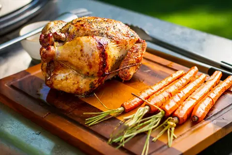 whole lemongrass grilled chicken with roasted carrots on wooden cutting board, outdoor setting