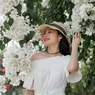 woman in white off-shoulder dress and dressy casual sun hat (straw with black band) surrounded by white bougainvillea flowers